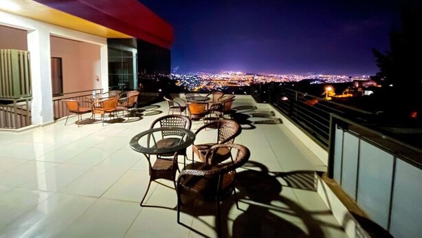 An outdoor terrace with wicker furniture and a city view at night. - Rebero View Apartments (Kigali)