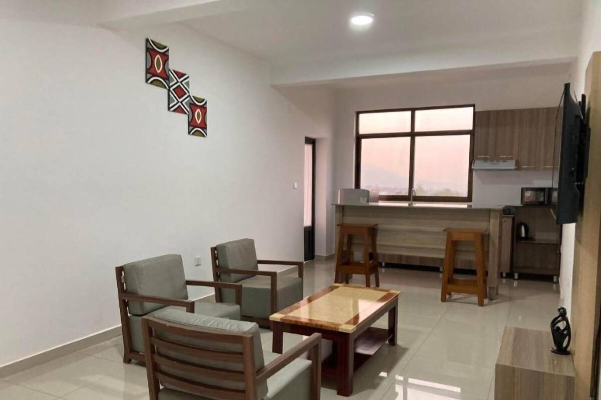 A modern living room with a sofa set, a coffee table, and a kitchen area with a window.