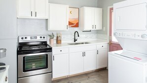Une cuisine moderne avec des meubles blancs, une cuisinière en acier inoxydable, un évier et un lave-linge blanc.