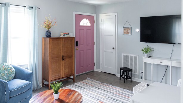 Un salon avec un canapé bleu, un meuble en bois, une porte rose, une porte blanche, un téléviseur et une petite table sur laquelle se trouve une plante.
