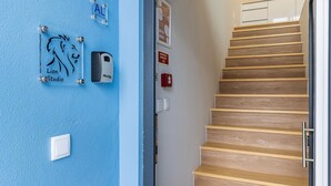 A staircase with wooden steps and a handrail, a blue wall with a lion logo and a doorbell, and a fire alarm on the wall. - Noah's Ark by LovelyStay (Cascais)