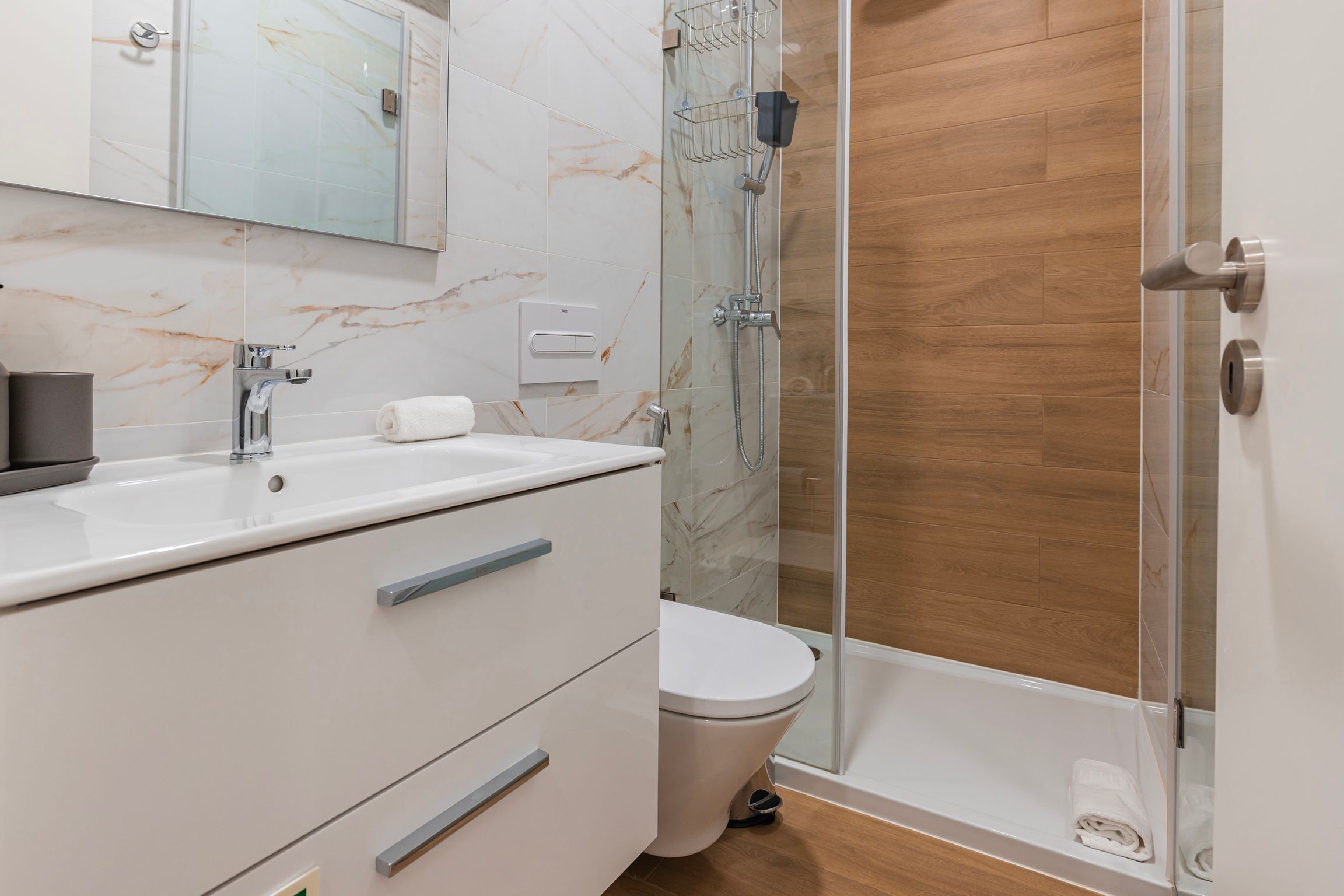 Un baño moderno con tocador de baldosas de mármol, cabina de ducha de vidrio y suelo de madera.