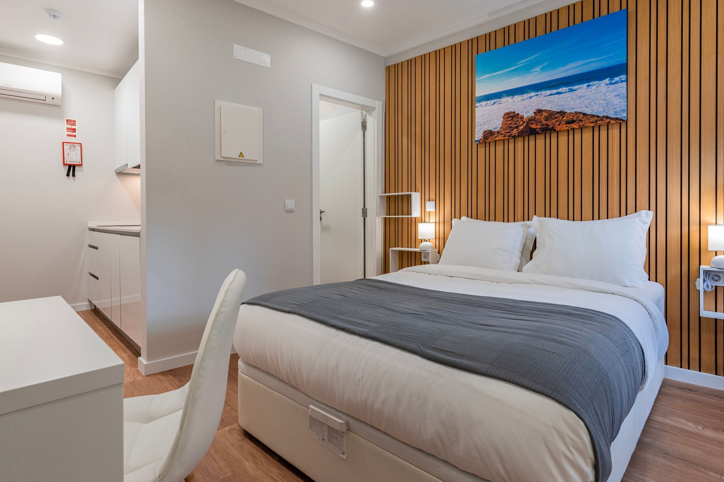 A modern bedroom with a bed, bedside tables, and a wooden panel wall with a painting.