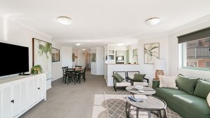 A modern living room with a television, dining area, kitchen, and a green sofa. - Golden Sea 12 - Absolute Beachfront Bilinga - Min. 3 Night Stays! (Bilinga)