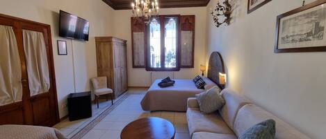 A hotel room with a large bed, a sofa, a wooden table, a TV, a chandelier, and a wardrobe.