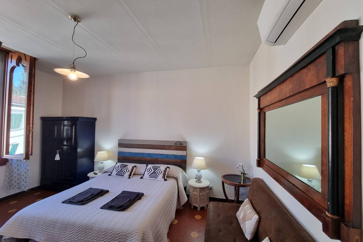 A hotel room with a bed, bedside tables, a wardrobe, a mirror, and a window.