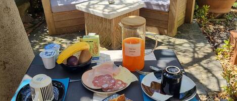 An outdoor dining area with a table set for breakfast, including bread, fruit, and a beverage.