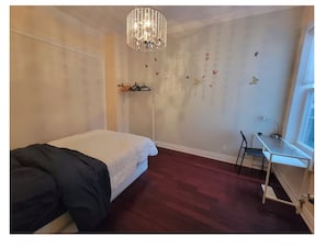 Een slaapkamer met een bed, bureau, stoel, een kroonluchter en vlinderstickers op de muur.