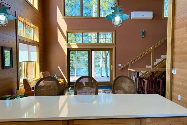 A dining area with a large table, chairs, and a view of trees through the windows. - Lake front NEW Cabin 2bd 2b AC/WIFI, kayak, beach, fish, firepit (Rhinelander)