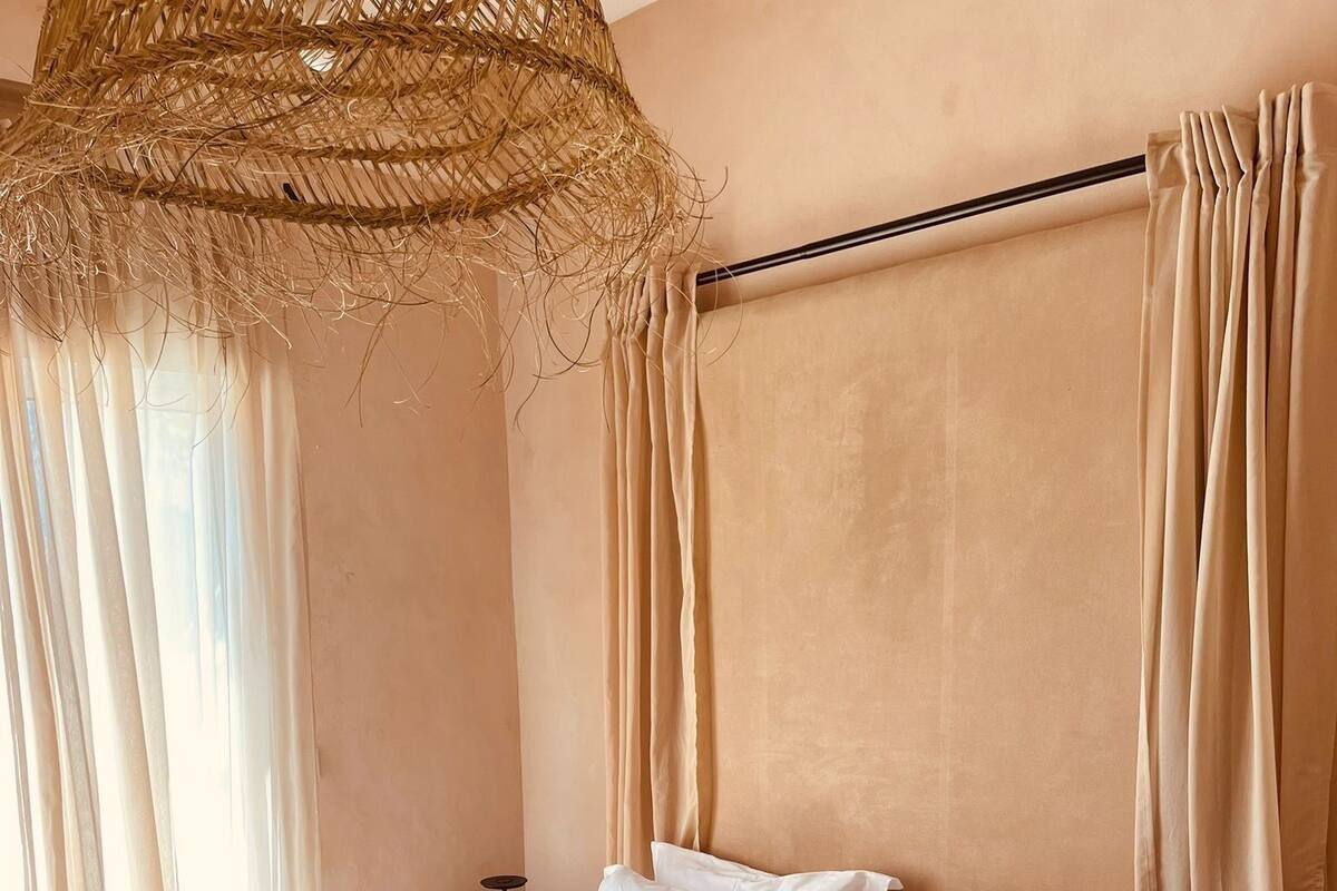 A neatly made bed with white and beige bedding, a striped blanket, and a woven headboard.