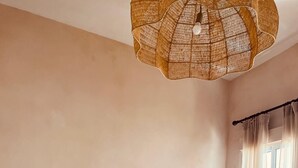 Una camera da letto con un letto grande, due comodini con lampade, un lampadario in rattan sospeso e tende leggere su una finestra.