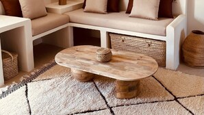 A modern living room with a sectional sofa, a round wooden coffee table, a woven hanging light fixture, and a small side table with a lamp. - Templo Sotogrande (San Roque)