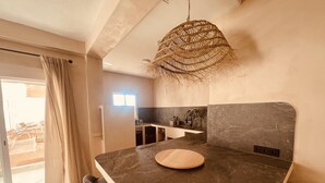 Una cucina moderna con piani di lavoro in marmo scuro, un tavolo rotondo in legno e un lampadario intrecciato.