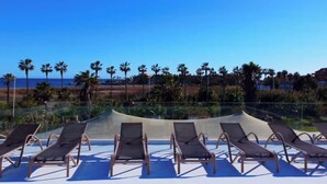 Area piscina con lettini e vista sull'oceano e palme.