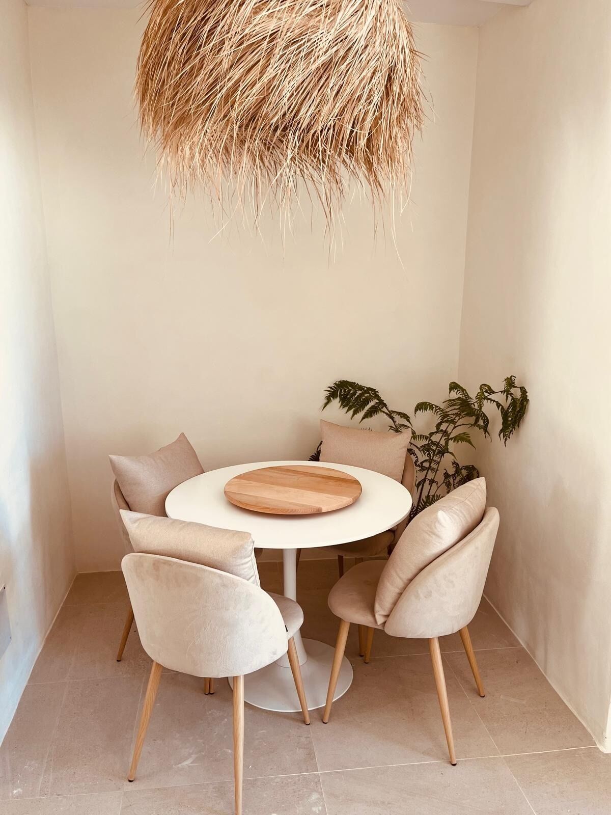 Un coin repas comprenant une table ronde, quatre chaises, une planche en bois et un luminaire suspendu.