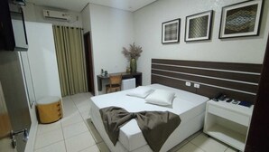 Quarto de hotel com cama, mesa de cabeceira e escrivaninha com cadeira.