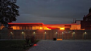 Un edificio moderno con fachada iluminada en rojo, un camino de grava y una cerca de madera.
