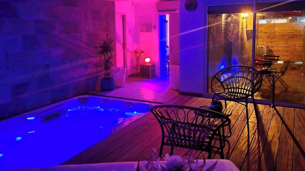 Un área de piscina interior moderna con una terraza de madera, un jacuzzi y un espacio de descanso con sillas.