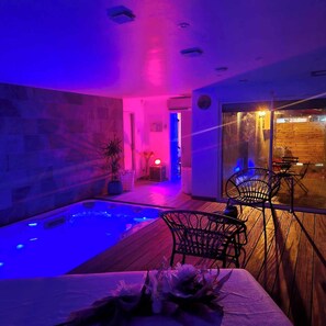 A modern indoor pool area with a wooden deck, a hot tub, and a seating area with chairs. - Gite Love Room and Spa, a romantic getaway in Saint-Omer (Saint-Omer)