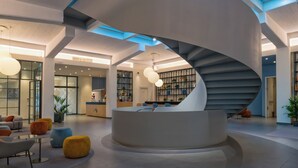 Un intérieur moderne avec un escalier en colimaçon central, un comptoir d’accueil et des espaces de détente.