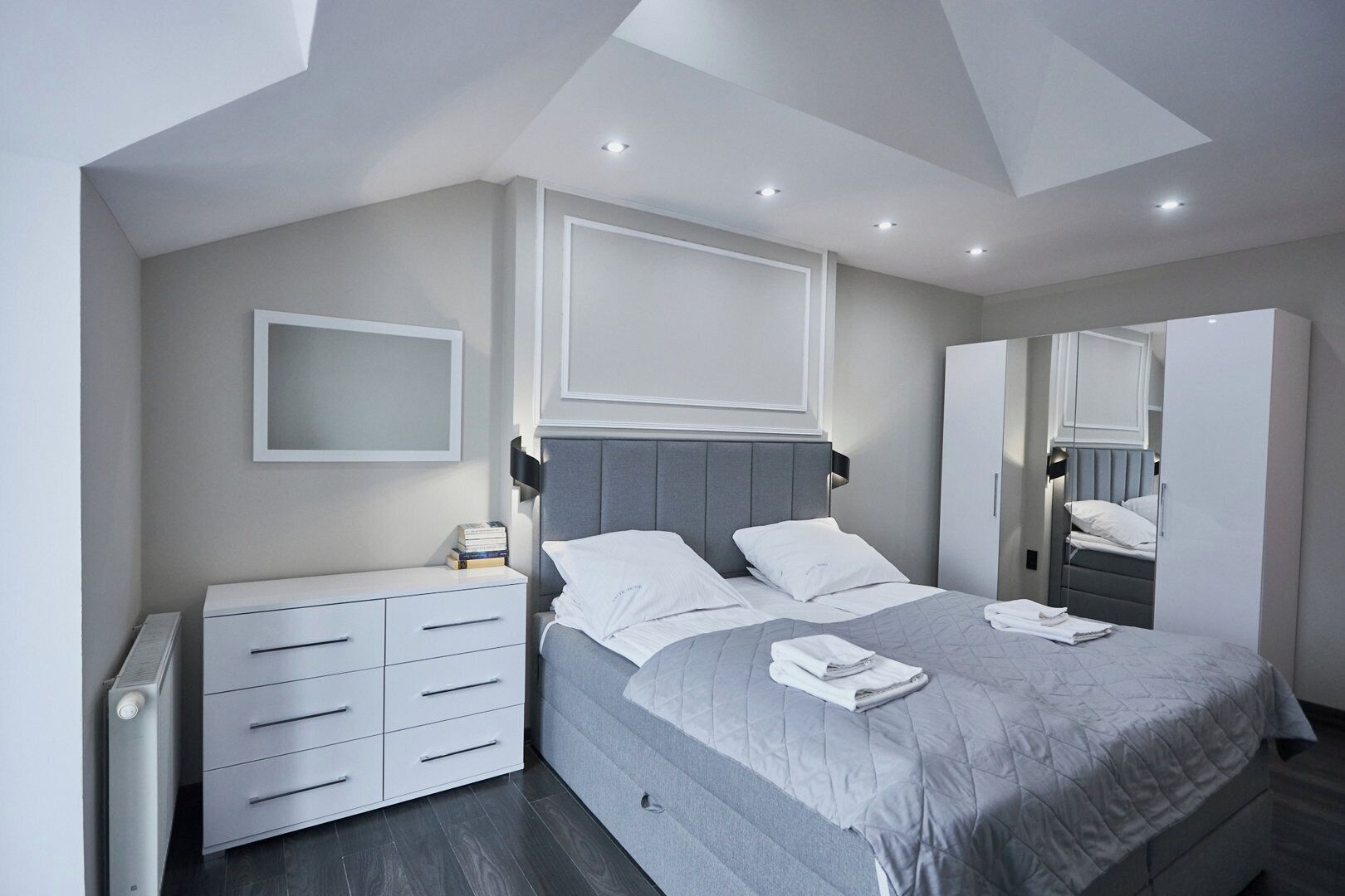 Ein modernes Schlafzimmer mit einem Bett, Nachttischen, einer Kommode und einem großen Spiegel.