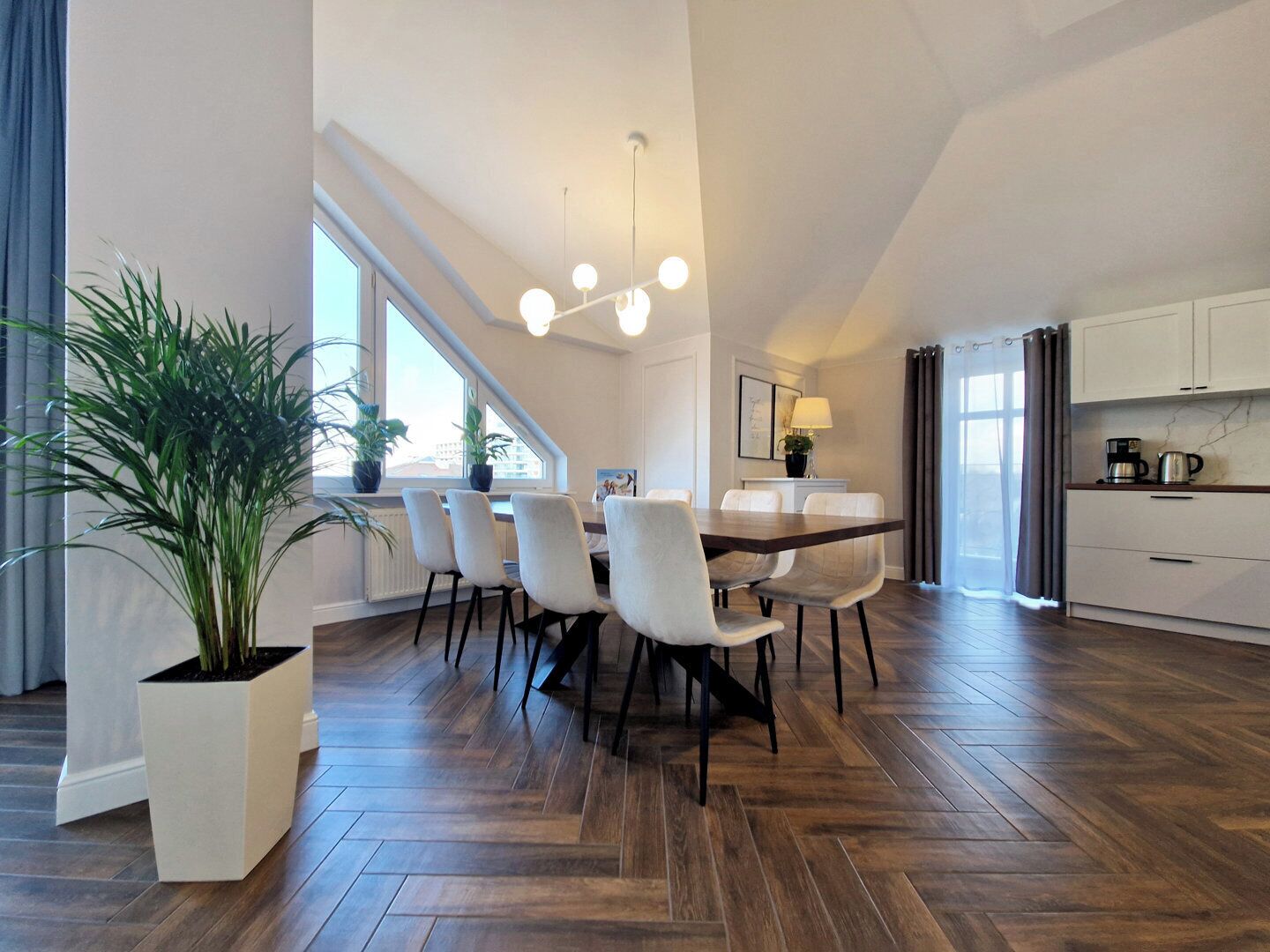 A modern kitchen with white cabinets, a dining area with a wooden table and chairs, and a large window providing natural light.