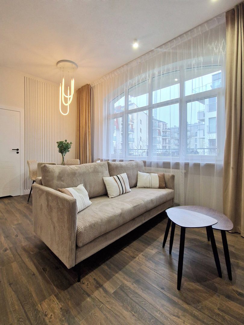 A modern living room with a sofa, a small table, and a large window with curtains.