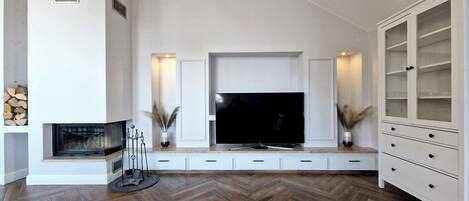 Uma sala de estar moderna com uma grande TV de tela plana, estantes embutidas e piso de madeira em padrão herringbone.