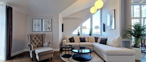 A modern living room with a herringbone wood floor, a tufted armchair, a white sectional sofa, and a round coffee table.