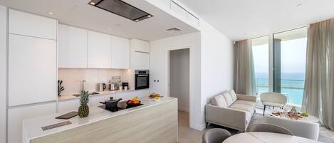A modern kitchen with white cabinets, a central island with fruits, and a dining area with a marble table.