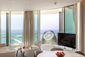 A modern living room with a large TV, comfortable seating, a dining table, and a view of the sea and marina. - Ayia Napa Marina East Tower Suite (Ayia Napa)