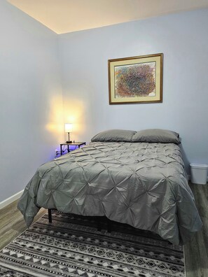 Ein Schlafzimmer mit einem Bett, einem Teppich, einem Wandbild und einem Nachttisch mit einer Lampe.
