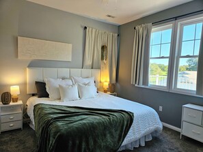 A bedroom with a bed, nightstands, a wall-mounted artwork, and a window with curtains. - New 7 Bedroom Home On Beautiful Blackthorn Golf Club (South Bend)