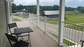 A covered porch with a table and chairs, overlooking a green landscape and buildings. - Brand New Home On Beautiful Blackthorn Golf Club (South Bend)