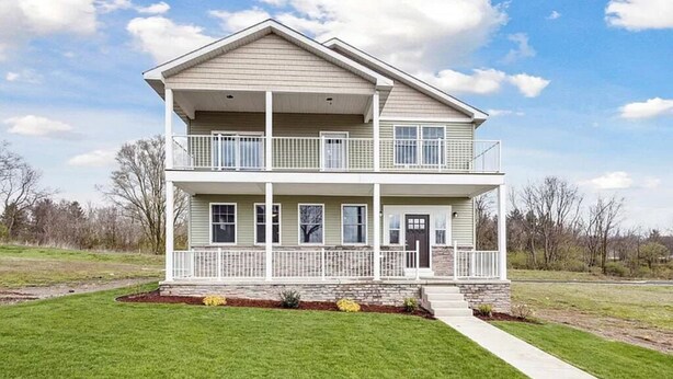A two-story house with a balcony on the upper floor, a front porch, and a well-maintained lawn. - Brand New Home On Beautiful Blackthorn Golf Club (South Bend)