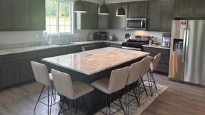 A modern kitchen with a large island, dark cabinets, stainless steel appliances, and pendant lighting. - Brand New Home On Beautiful Blackthorn Golf Club (South Bend)