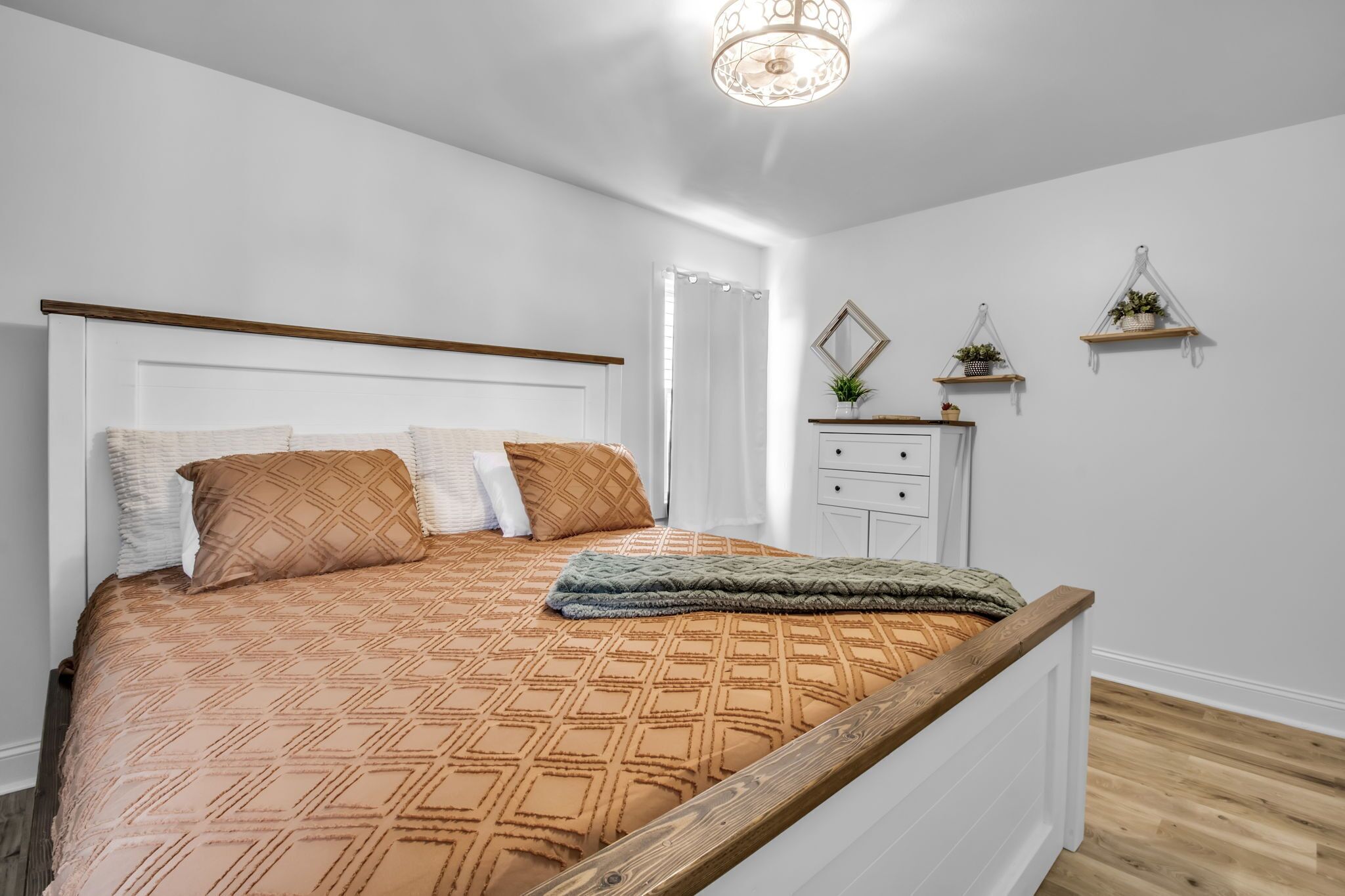 A bedroom with a wooden bed frame, a patterned bedspread, and a bedside table with a mirror and shelves.
