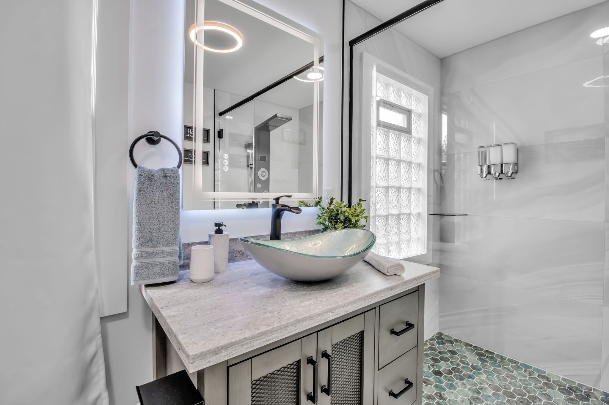 A modern bathroom with a glass sink, a large mirror, and a shower area.