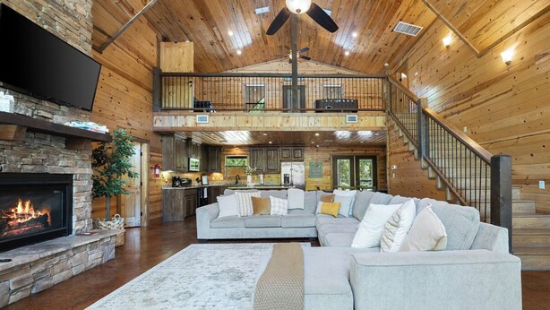 A spacious living room with a fireplace, a large gray sectional sofa, and a staircase leading to an upper level.