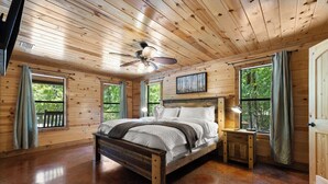 A wooden cabin bedroom with a bed, a ceiling fan, and large windows.