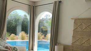 A bedroom with a bed, a bench, a nightstand, and a view of a swimming pool. - Charming Villa Son Parc (Son Parc)