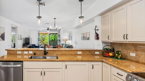 Cocina moderna con gabinetes blancos, encimeras de granito, electrodomésticos de acero inoxidable e iluminación colgante.