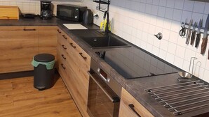 Moderni keittiö, jossa on puukalusteet, musta työtaso, sisäänrakennettu uuni ja kahvinkeitin.