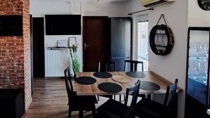 Ruokailutila, jossa on puinen pöytä ja mustat tuolit, tiiliseinä sekä ovi, joka johtaa toiseen huoneeseen.