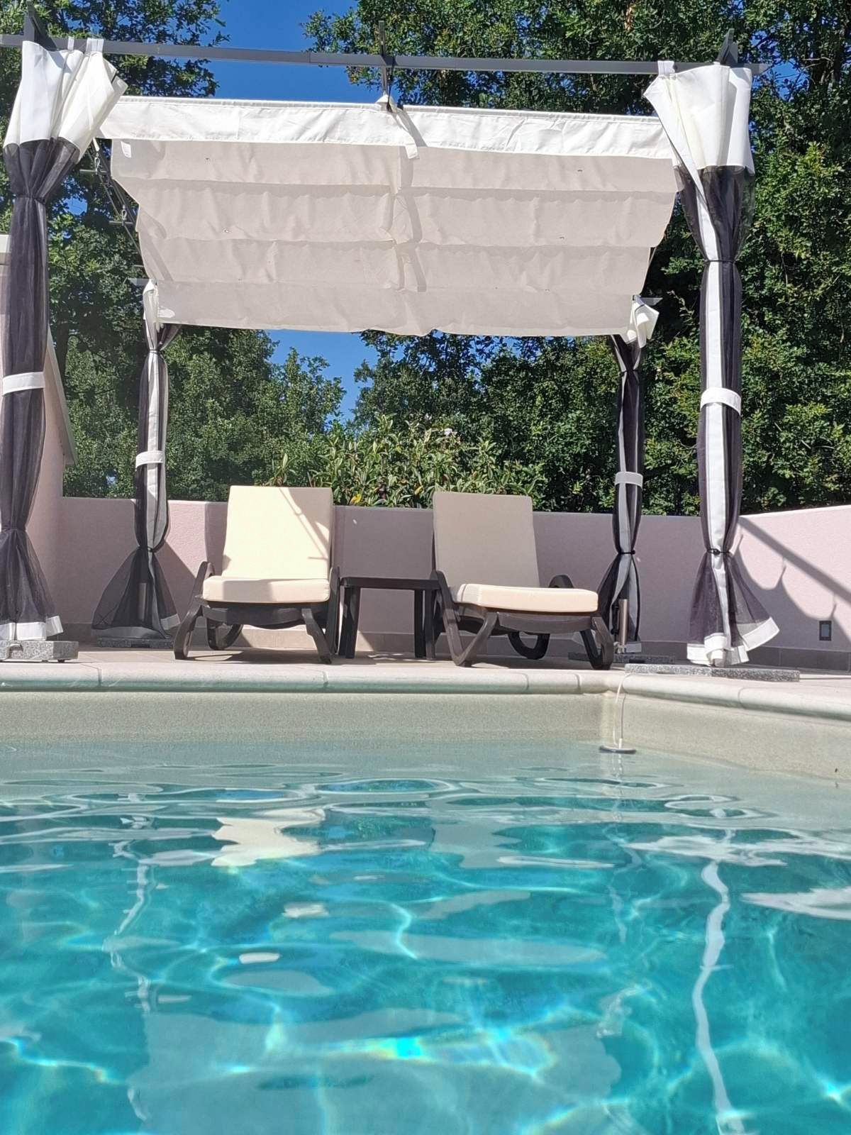 A poolside area with a covered seating area and lounge chairs.