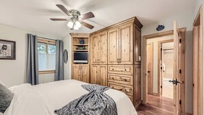 Una camera da letto con un letto, una ventola a soffitto, mobili in legno e l'ingresso del bagno.