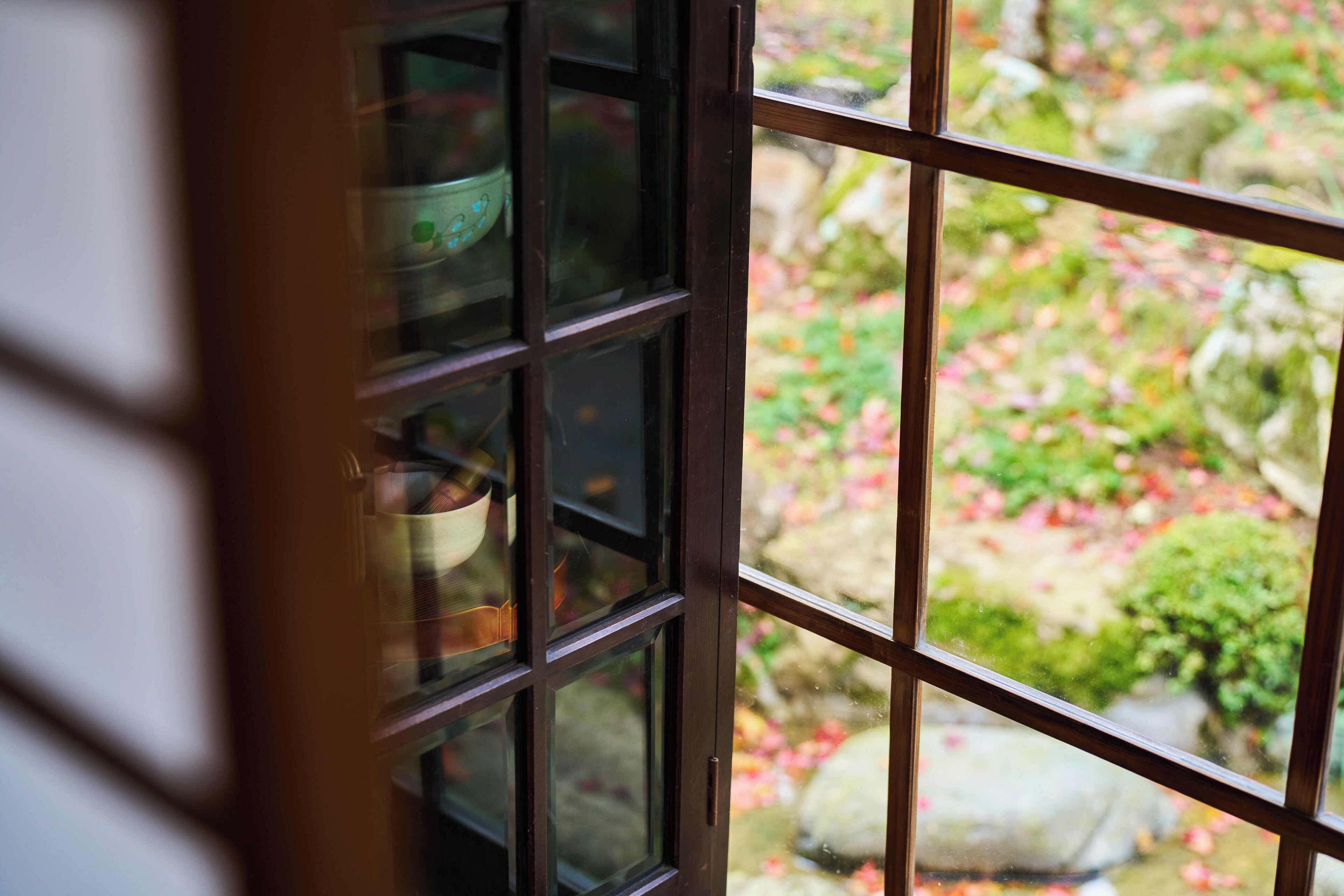 Vista a través de una ventana con diseño de cuadrícula, mostrando un jardín con rocas y follaje.