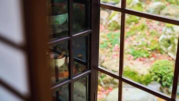 Vista a través de una ventana con diseño de cuadrícula, mostrando un jardín con rocas y follaje.