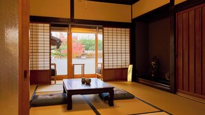 Um quarto japonês tradicional com tatames, uma mesa de madeira baixa e portas deslizantes que dão para um jardim externo.