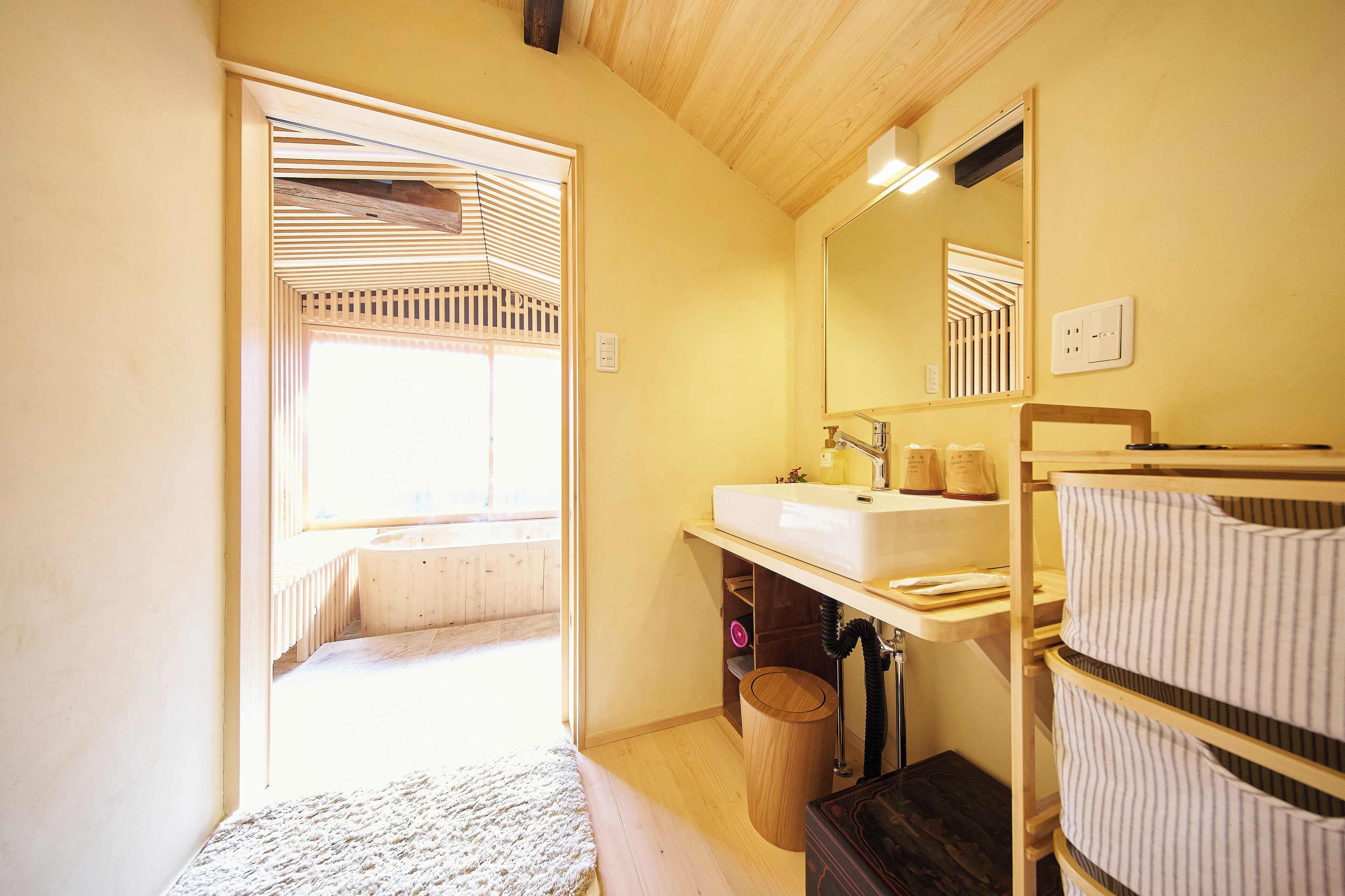 Une petite salle de bain avec un plancher en bois, un lavabo, un miroir et une fenêtre avec des stores.